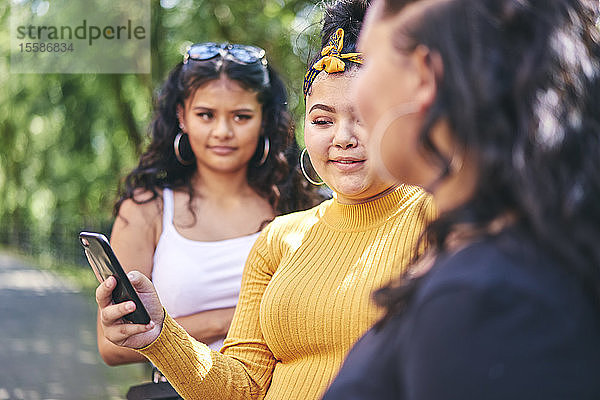 Junge Frau mit Schwestern im Teenageralter schaut auf Smartphone am Park  Blick über die Schulter
