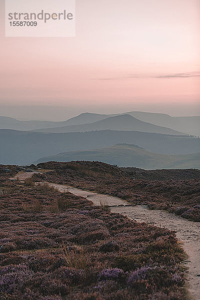 Ein Weg im Peak-District-Nationalpark  der zu den Bergen im Hintergrund mit einem schönen rosa Himmel führt  Peak District  Derbyshire  England  Vereinigtes Königreich