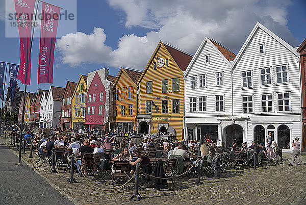 Touristen sitzen in der Sonne in den Bars und Cafés im Freien am alten Kai und in den traditionellen Holzhäusern im Bryggen-Viertel von Bergen  UNESCO-Weltkulturerbe  Norwegen  Skandinavien