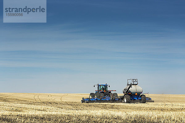 Traktor mit Einzelkornsämaschine auf einem Feld mit blauem Himmel und dunstigen Wolken  in der Nähe von Beiseker; Alberta  Kanada