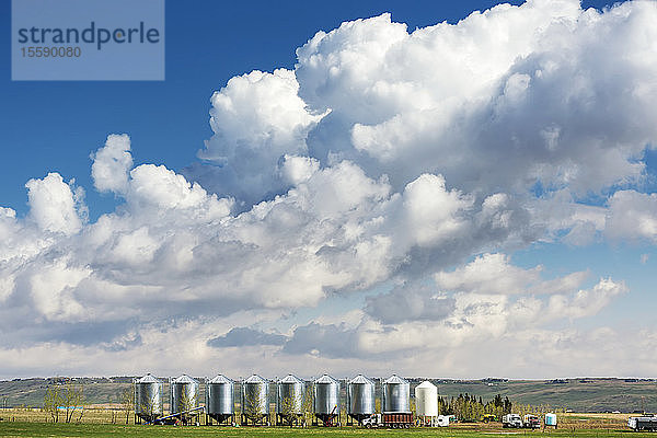 Eine Reihe großer Getreidespeicher aus Metall mit dramatischen Gewitterwolken und blauem Himmel im Hintergrund  westlich von Calgary; Alberta  Kanada