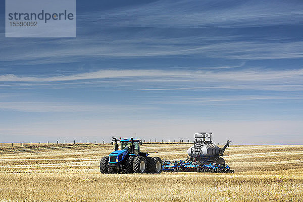 Traktor mit Einzelkornsämaschine  Aussaat eines Stoppelfeldes bei blauem Himmel und dunstigen Wolken  in der Nähe von Beiseker; Alberta  Kanada