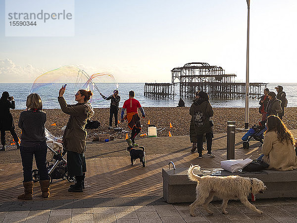 Herstellung von Seifenblasen auf der Strandpromenade mit Menschen und Hunden  die zusehen  und West Pier im Hintergrund; Brighton  East Sussex  England