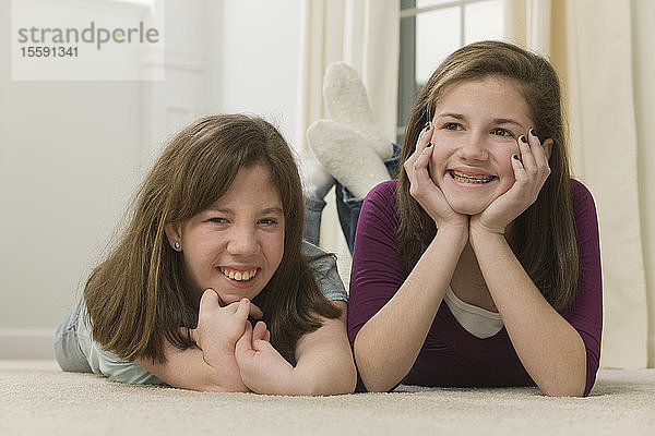 Zwei Teenager-Mädchen liegen zusammen und lächeln  Teenager-Mädchen mit Geburtsfehler im Gespräch mit einem Mobiltelefon