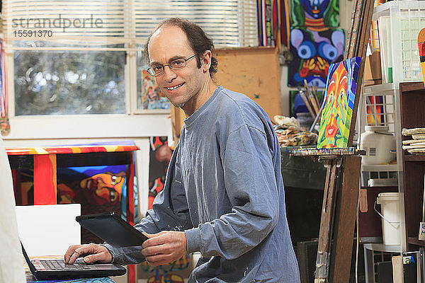 Mann mit Asperger-Syndrom bei der Arbeit an seinem Tablet und Computer in seinem Kunstatelier
