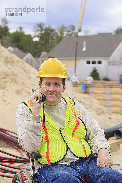 Bauleiter mit Querschnittslähmung am Walkie Talkie mit Fundament und Rohren im Hintergrund