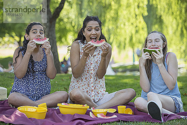 Glückliche hispanische Familie beim Picknick und beim Verzehr von Wassermelonen in einem Park