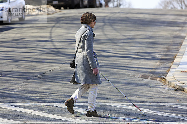 Junge blinde Frau  die mit ihrem Stock die Straße überquert