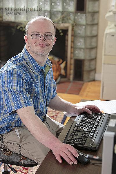 Mann mit Down-Syndrom bei der Arbeit an seinem Computer in einem Büro