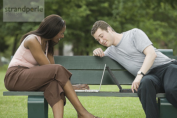 Mid adult couple sitting on a park bench and using laptops
