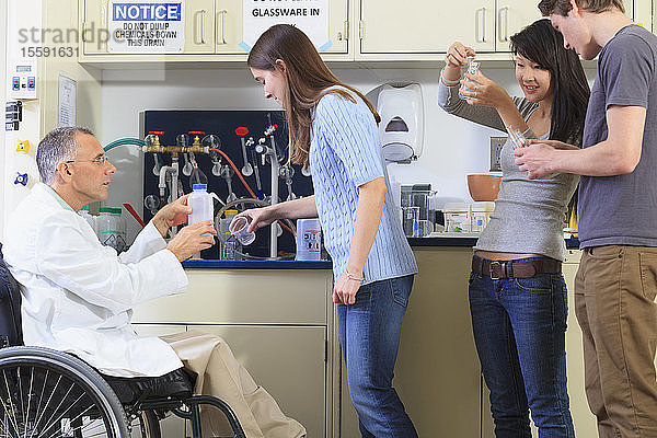 Professor mit einer Rückenmarksverletzung im Rollstuhl im Gespräch mit Studenten der Ingenieurwissenschaften über Laborgeräte aus Glas