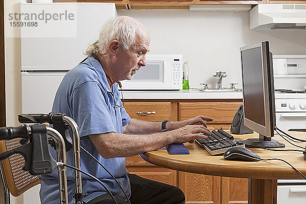 Mann mit Ataxie  der mit seiner Gehhilfe in der Küche an seinem Computer arbeitet