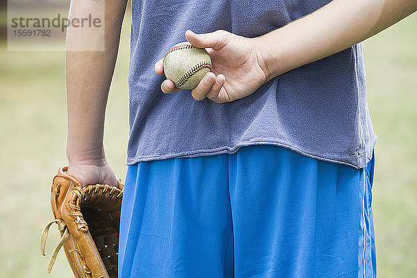 Mittelansicht eines Teenagers  der einen Baseball hinter seinem Rücken versteckt