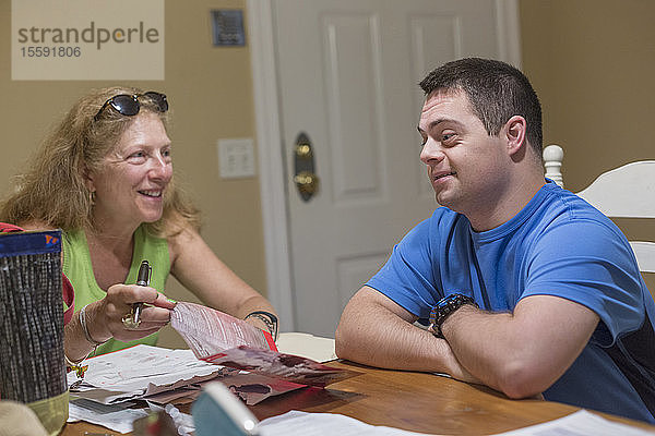 Mann mit Down-Syndrom sitzt neben seiner Mutter und bezahlt Rechnungen