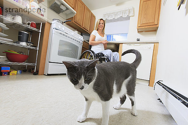 Frau mit einer Rückenmarksverletzung in ihrer barrierefreien Küche mit ihrer Katze