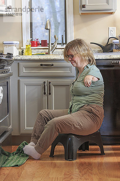 Frau mit TAR-Syndrom  die ein Küchenhandtuch mit den Füßen aufhebt