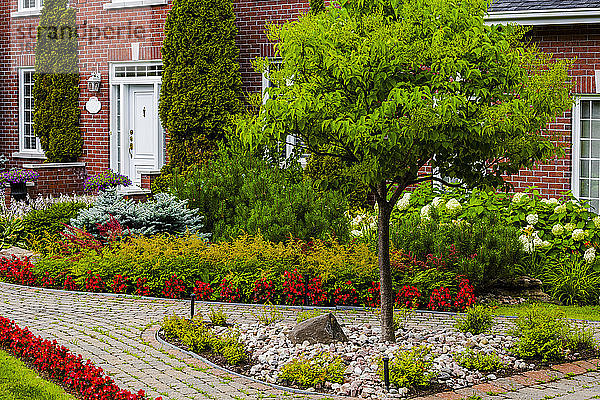 Stattliches Backsteinhaus mit einem gewundenen Weg und einer Gartenanlage mit Pflanzen und Blumen im Vorgarten; Hudson  Quebec  Kanada