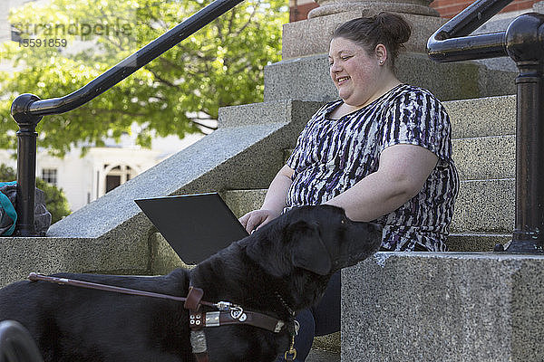 Frau mit Sehbehinderung sitzt mit ihrem Diensthund vor einem Computer