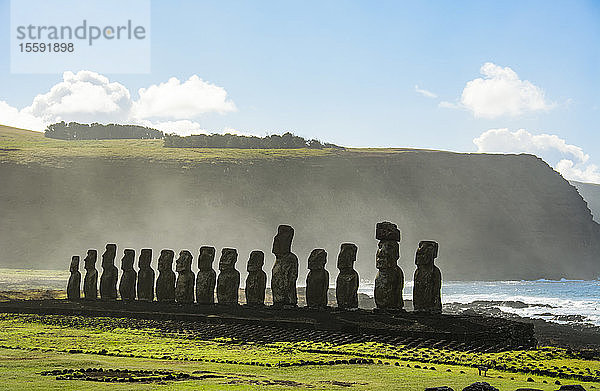 Die fünfzehn Moais von Tongariki aus der Ferne gesehen in abnehmender Perspektive gegen den Ozean und den blauen Himmel; Osterinsel  Chile