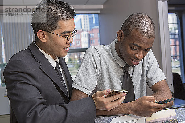 Zwei Männer mit Autismus schauen in einem Büro auf ihre Handys