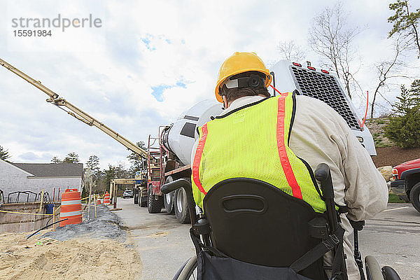 Bauleiter mit Querschnittslähmung am Walkie-Talkie zur Betonpumpe beim Gießen des Fundaments