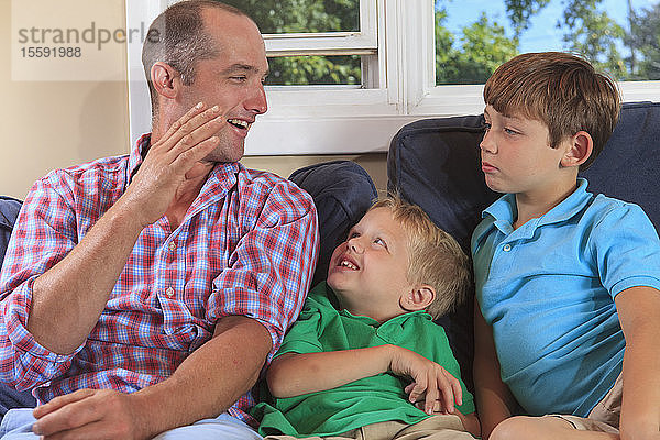 Vater und Söhne mit Hörbehinderung gebärden auf ihrer Couch ein B in amerikanischer Zeichensprache