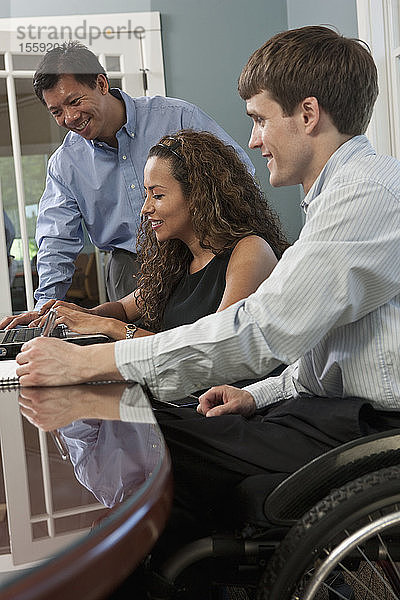 Ein Geschäftsmann mit einer Rückenmarksverletzung und eine sehbehinderte hispanische Geschäftsfrau benutzen einen Laptop in einem Büro