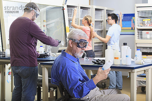 Ingenieurprofessor mit Muskeldystrophie betrachtet zusammen mit Studenten ein chemisches Reagenz in einem Chemielabor