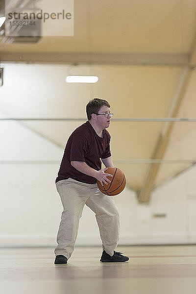 Junger Mann mit Down-Syndrom spielt Basketball in der Schulsporthalle