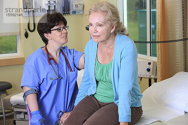Krankenschwester mit Cerebralparese an Stöcken prüft die Ohren eines Patienten in einer Krankenstation