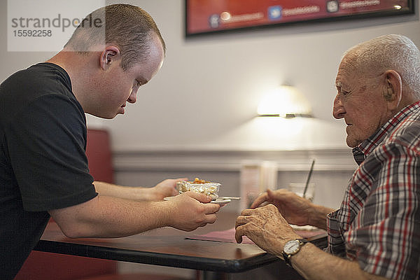 Kellner mit Down-Syndrom serviert einem Kunden in einem Restaurant das Essen