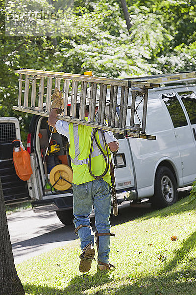 Ein Elektriker trägt eine Leiter zurück zu seinem Lastwagen