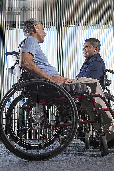 Zwei Männer mit Rückenmarksverletzungen in Rollstühlen unterhalten sich in einem Bürokorridor