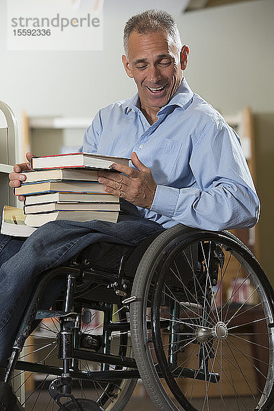 Mann im Rollstuhl mit einer Rückenmarksverletzung lässt Bücher aus einem Regal in einer Bibliothek fallen