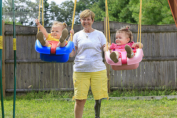 Großmutter mit Beinprothese spielt mit ihren Enkelkindern auf einer Schaukel