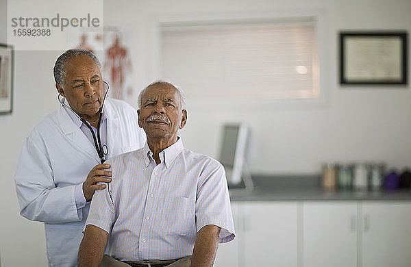 Ein älterer Mann lässt sich von einem männlichen Arzt in einem Büro den Herzschlag abhören.