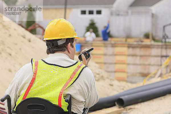 Bauleiter mit Querschnittslähmung am Walkie Talkie mit Fundament und Rohren im Hintergrund