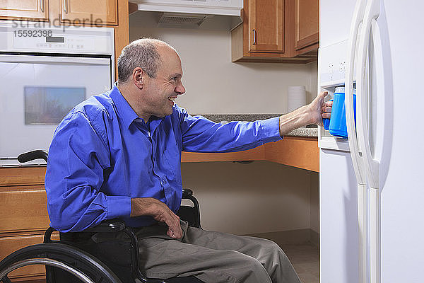 Mann mit Friedreich-Ataxie und deformierten Händen benutzt den Wasserspender in seinem Kühlschrank