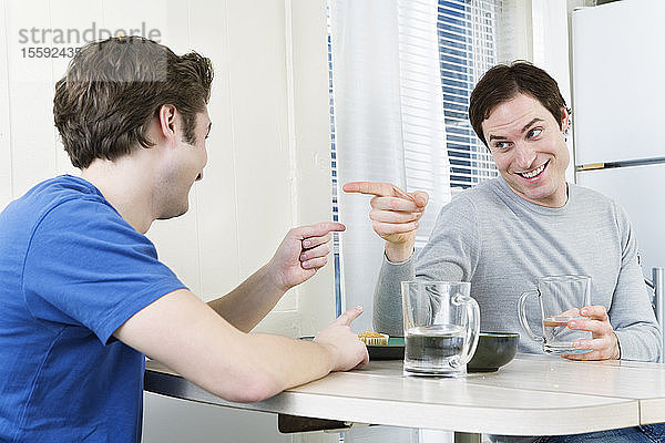 Zwei Männer  die am Esstisch mit dem Finger aufeinander zeigen.