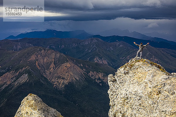 Sonnenschein beleuchtet einen Wanderer auf dem Gipfel des Sukakpak Mountain  während sich in der Ferne Sturmwolken über der Brooks Range zusammenbrauen; Alaska  Vereinigte Staaten von Amerika