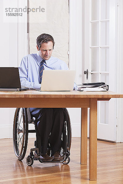 Geschäftsmann mit Querschnittslähmung im Rollstuhl bei der Arbeit an Laptops