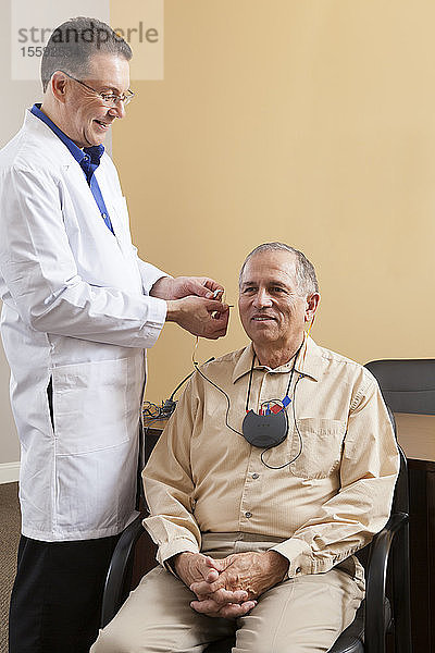Audiologe setzt Hinter-dem-Ohr-Hörgerät während der Programmierung in das Ohr eines Patienten ein