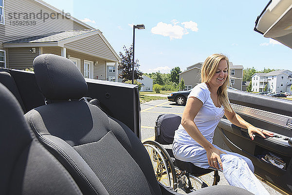 Frau mit Querschnittslähmung im Rollstuhl steigt in ihr adaptives Auto ein