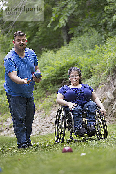 Frau mit Spina Bifida im Rollstuhl spielt Boccia mit ihrem Mann