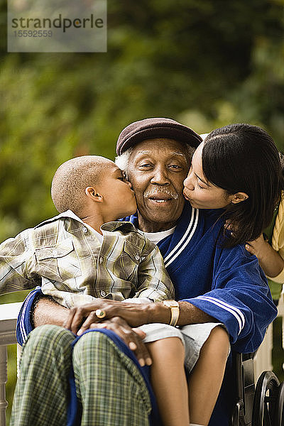 Ein älterer Mann  der im Rollstuhl sitzt  wird von seinem Enkel auf die Wange geküsst