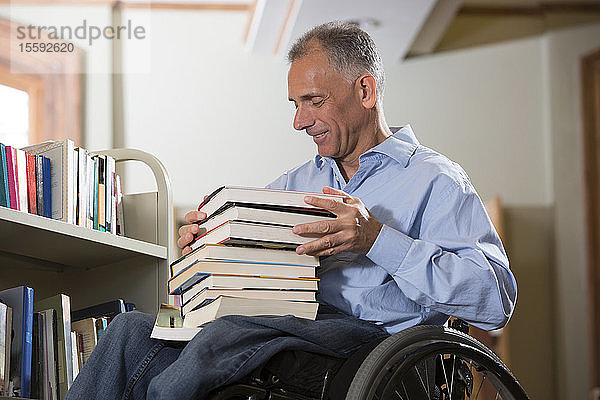 Mann im Rollstuhl mit einer Rückenmarksverletzung wählt Bücher aus einem Regal in einer Bibliothek aus