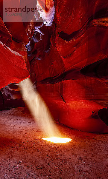 Upper Antelope Canyon mit einem Sonnenstrahl  der durch ein Loch  das einem Scheinwerfer ähnelt  auf den Boden scheint; Arizona  Vereinigte Staaten von Amerika