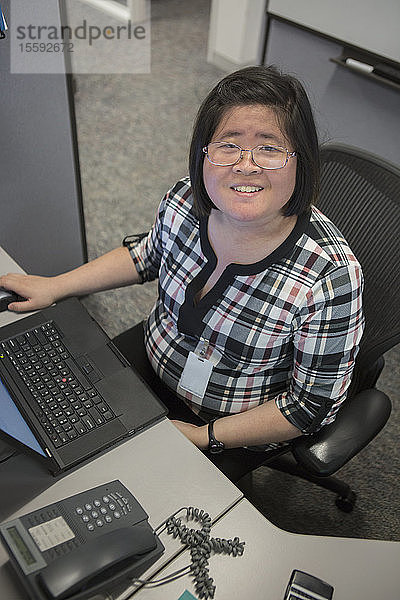 Asiatische Frau mit einer Lernbehinderung arbeitet an ihrem Computer im Büro