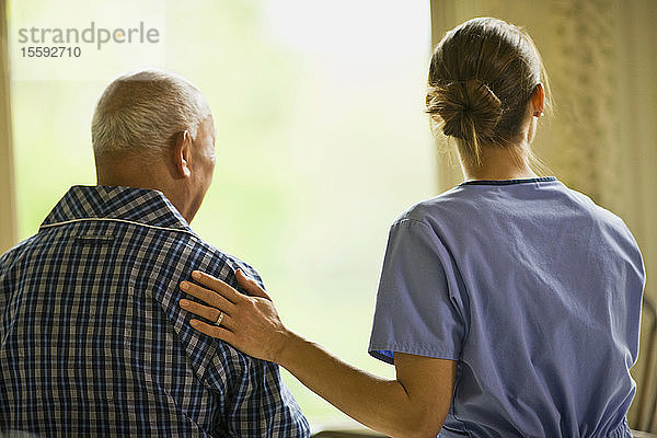 Eine Krankenschwester legt einem Mann beruhigend die Hand auf den Rücken.