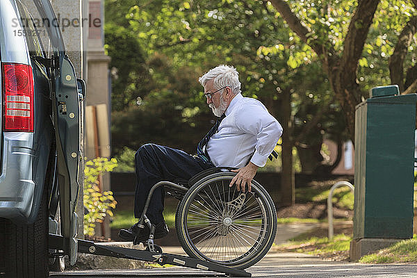 Geschäftsmann mit Muskeldystrophie im Rollstuhl beim Einsteigen in seinen behindertengerechten Lieferwagen auf dem Parkplatz